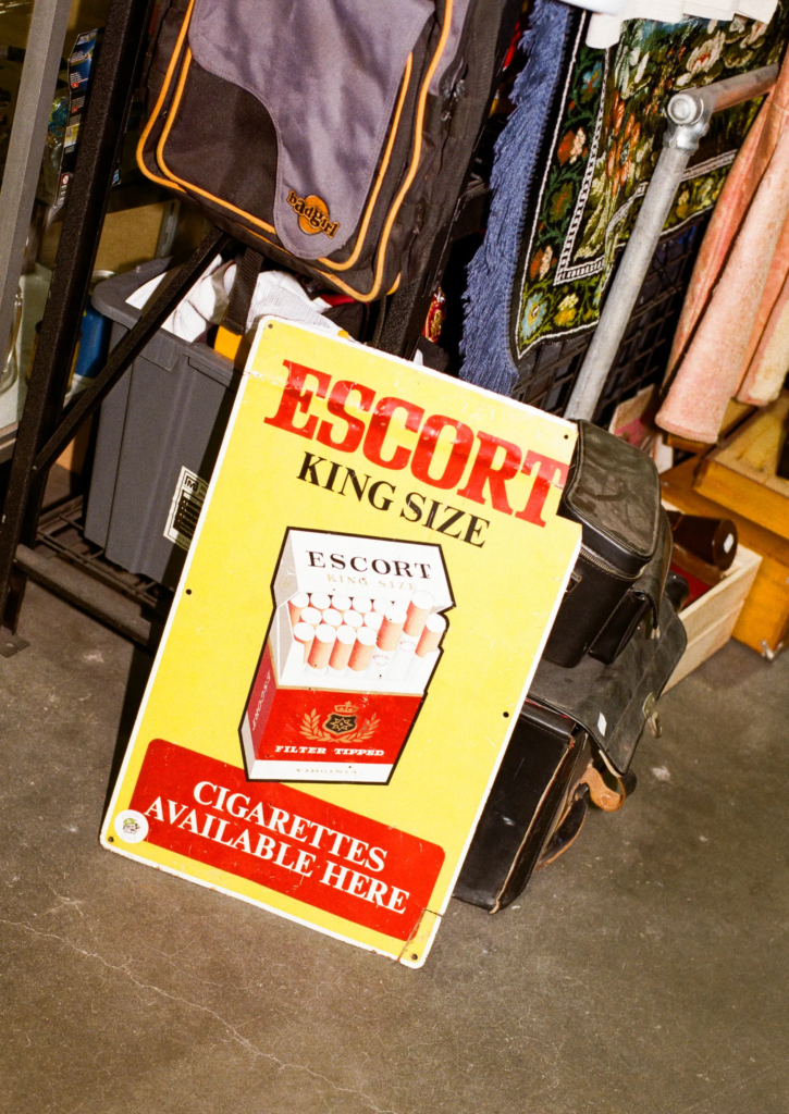 Vintage yellow advertising sign leaning beside bags, textiles and retro homewares in the Scrapdogs area