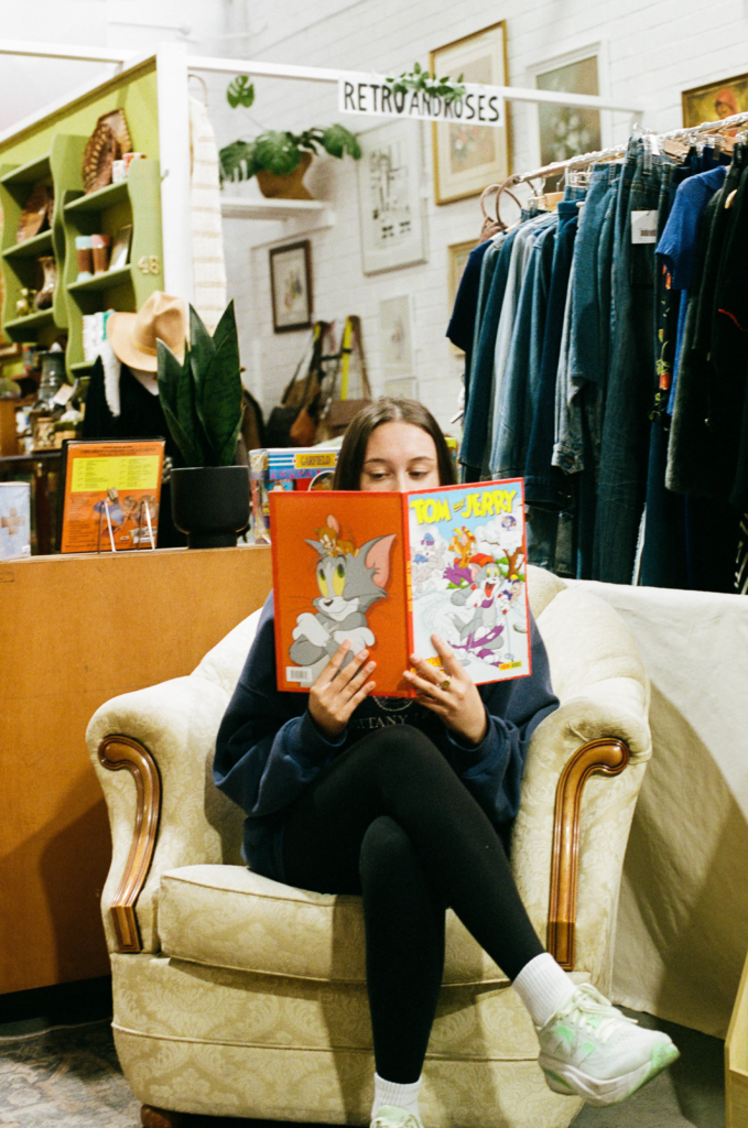 Person reading a Tom and Jerry book in vintage armchair at My Dead Grandpa Adelaide
