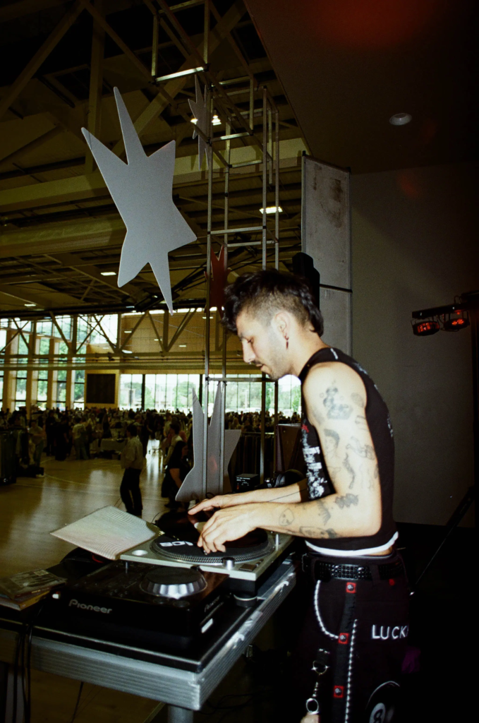 ALOT crew member DJing at a busy vintage market event with turntables and Y2K streetwear.