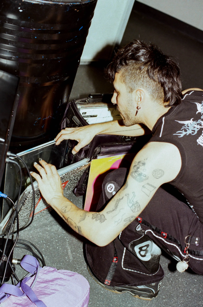ALOT owner Franki sorting records beside DJ equipment at a vintage market event, wearing Y2K rave inspired streetwear.