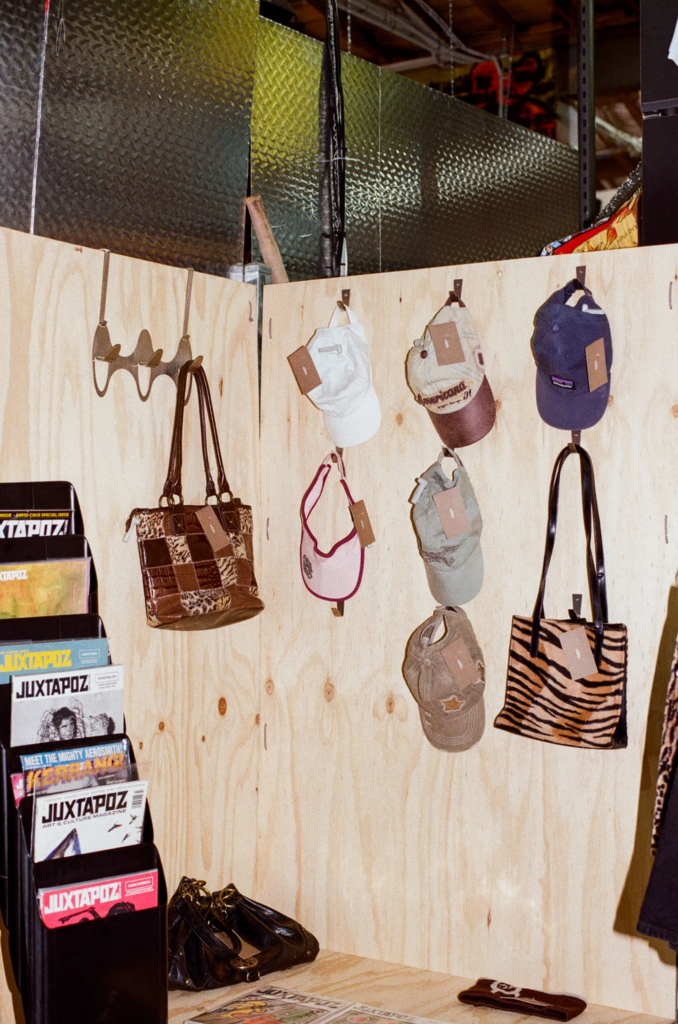 Vintage caps and patterned handbags displayed on a plywood wall in the Juno stall