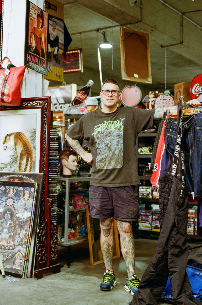 Scrapdogs owner Simon standing in a vintage stall with clothing, framed art, retro signs and collectibles in Adelaide