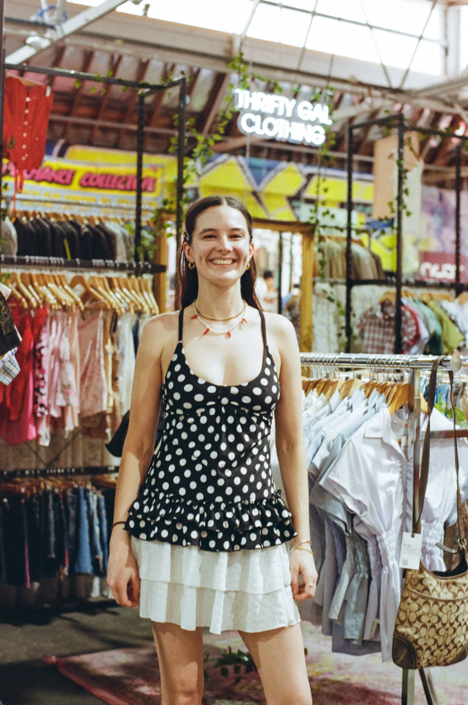 Liv from Thrifty Gal smiling in front of racks of Y2K tops and preloved clothing at MDG Adelaide.